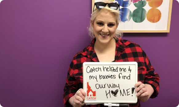 A woman holding a sign that says, “CATCH helped me and my babies find our way home!”